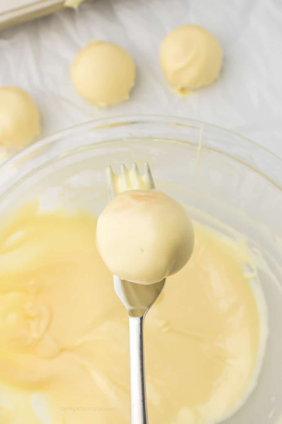 Lemon truffle being dipped in a bowl of white chocolate using a fork