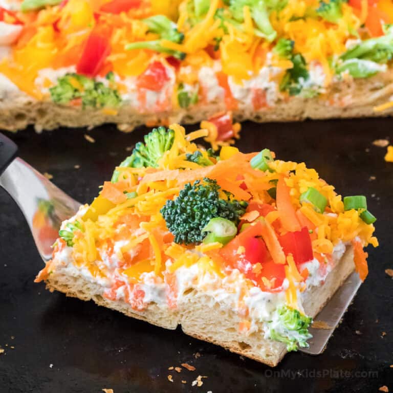 Cold veggie pizza slice on the pan at an angle being pulled away with a spatula