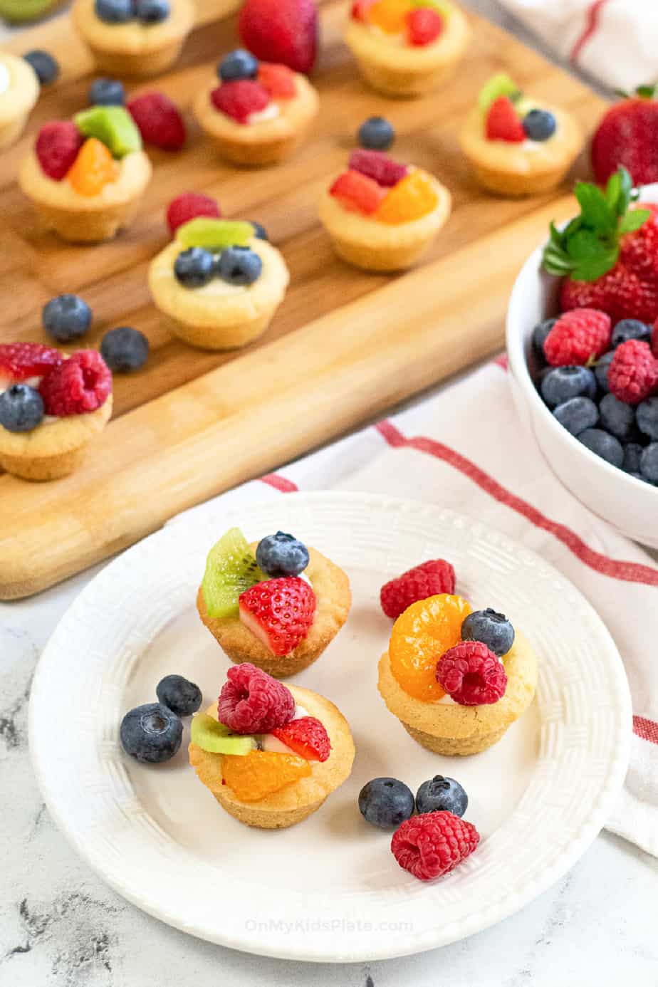 Cheesecake cookie cups topped with fruit on a plate and a wood board