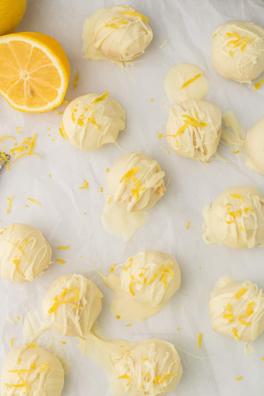 Lemon truffles from above on parchment paper coated in white chocolate topped with lemon zest