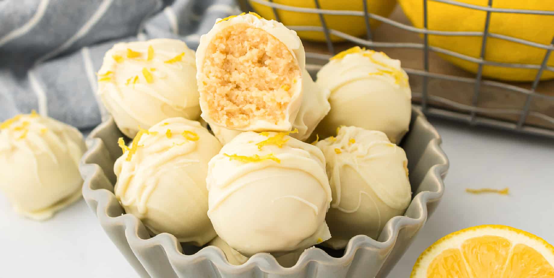 Wide side view of lemon truffles in a bowl with the top truffle missing a bite