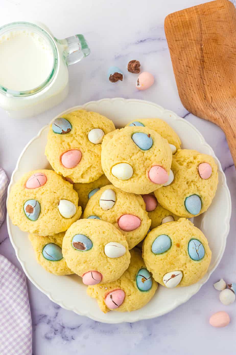 Cookies with mini chocolate eggs piled on a plate with a glass of milk from overhead