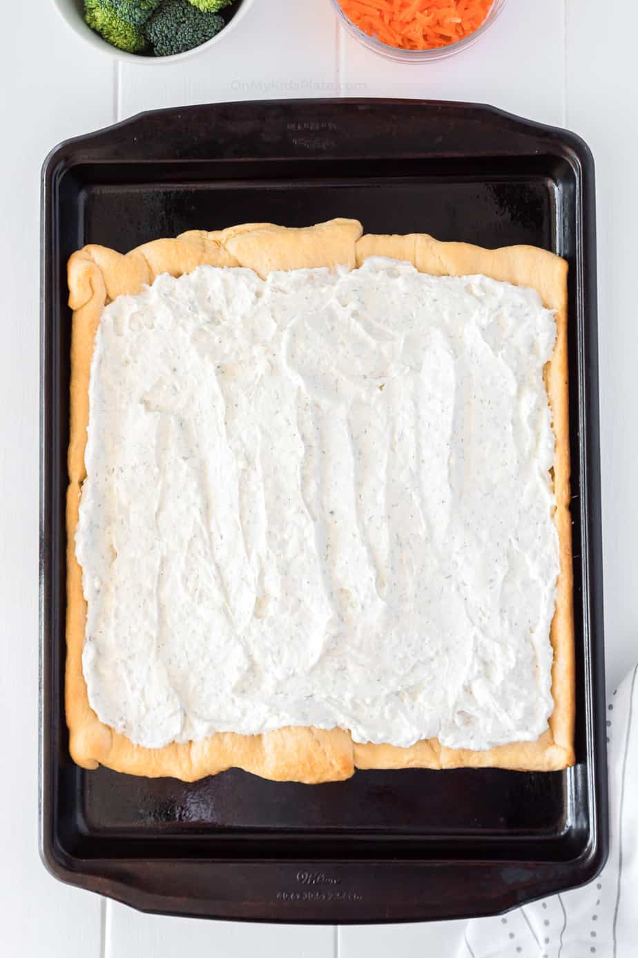 Flavored cream cheese spread onto crescent dough on a pan