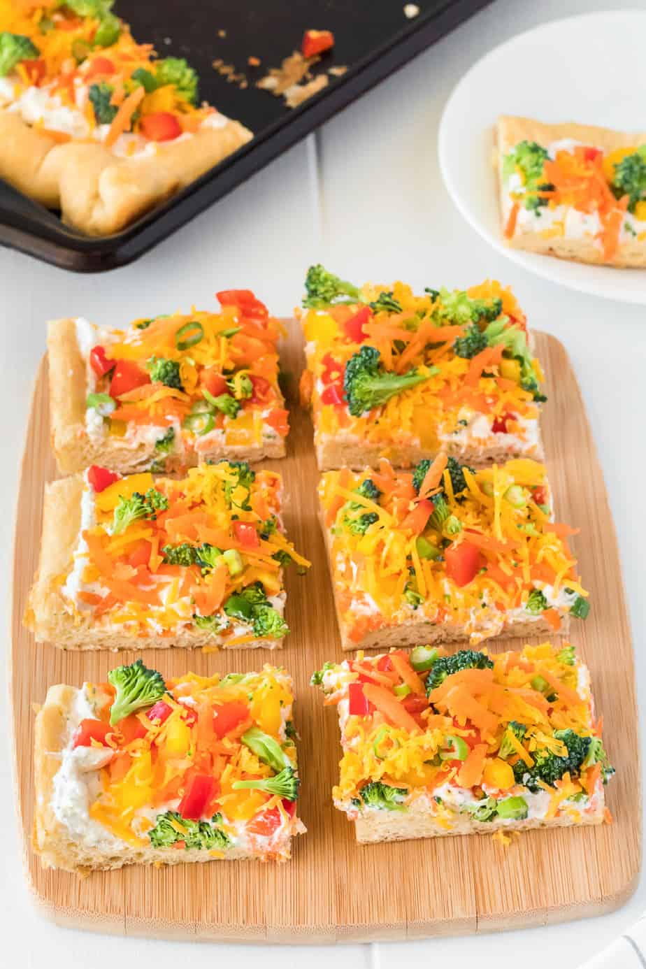 Cold veggie pizza slices on a cutting board with more on a pan in the background