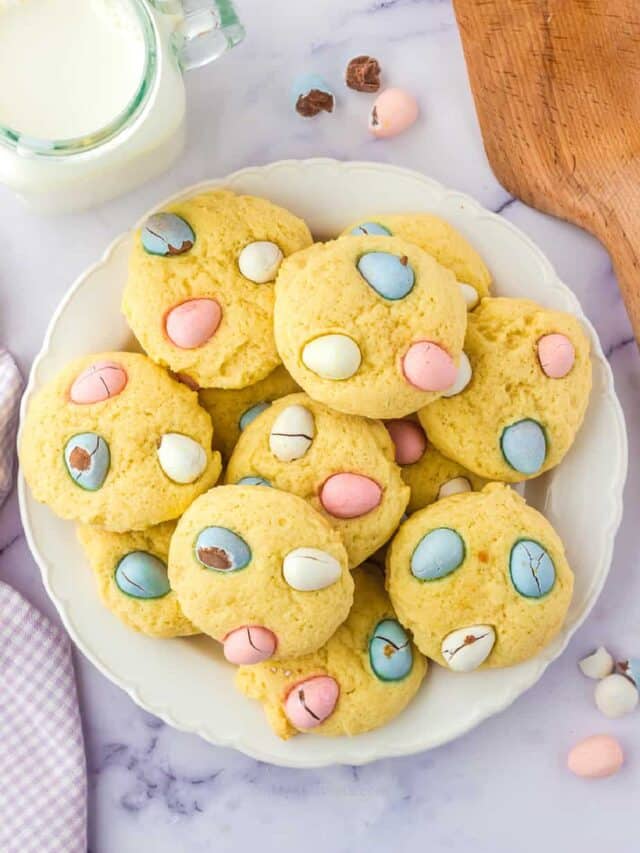 Cookies with mini chocolate eggs piled on a plate with a glass of milk from overhead