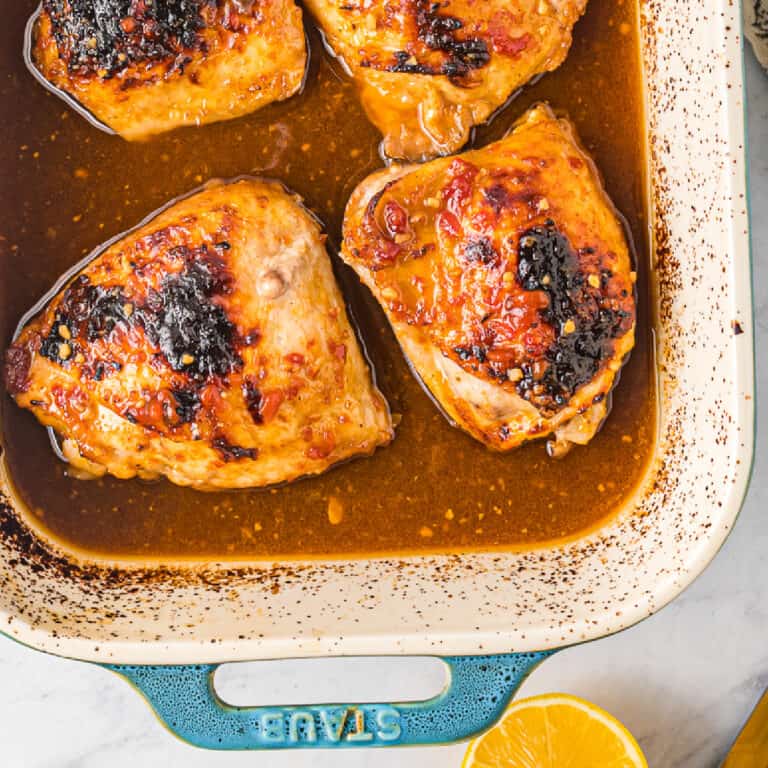 Close up of cooked chicken thighs in a honey garlic sauce in a baking pan from overhead