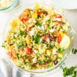 Mixed Greek Orzo salad with a wedge of lemon and feta cheese in a large bowl close up from overhead