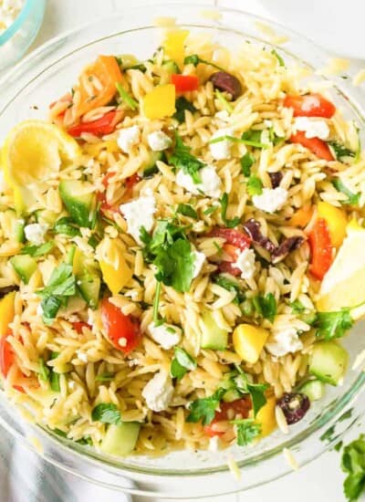 Mixed Greek Orzo salad with a wedge of lemon and feta cheese in a large bowl close up from overhead