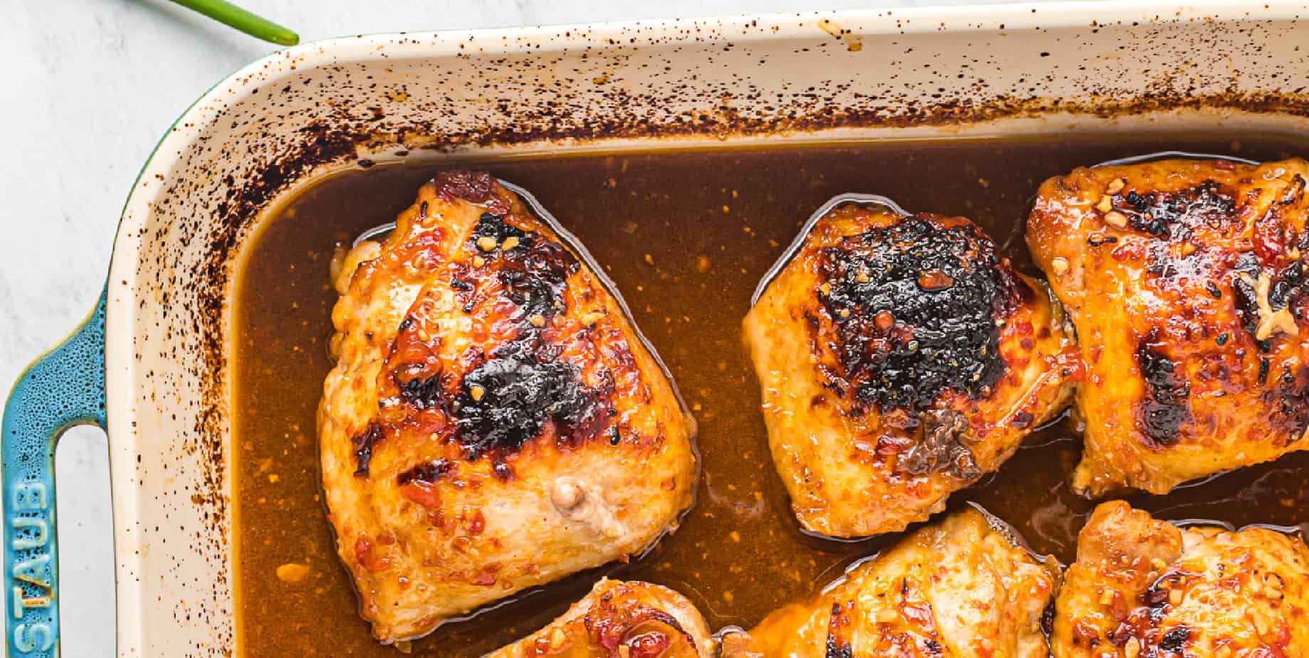 Honey garlic chicken thighs lined up in the edge of a baking dish.