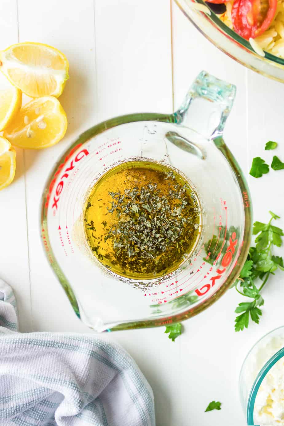 mixing oil lemon juice and dried herbs in a large glass measuring cup from above for dressing