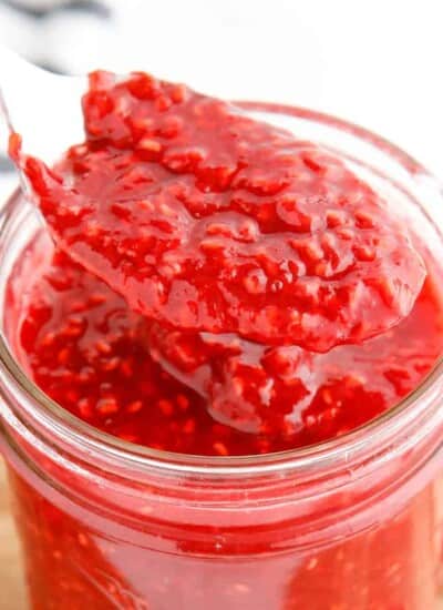 Close up side view of raspberry jam being lifted from a jar with a spoon cropped square