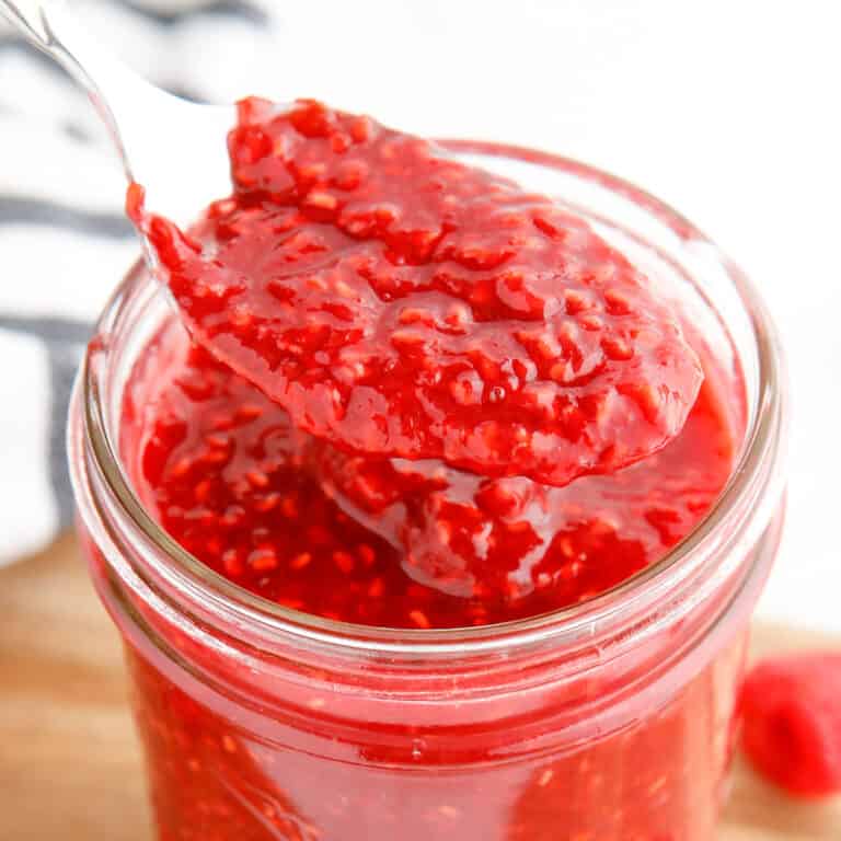 Close up side view of raspberry jam being lifted from a jar with a spoon cropped square