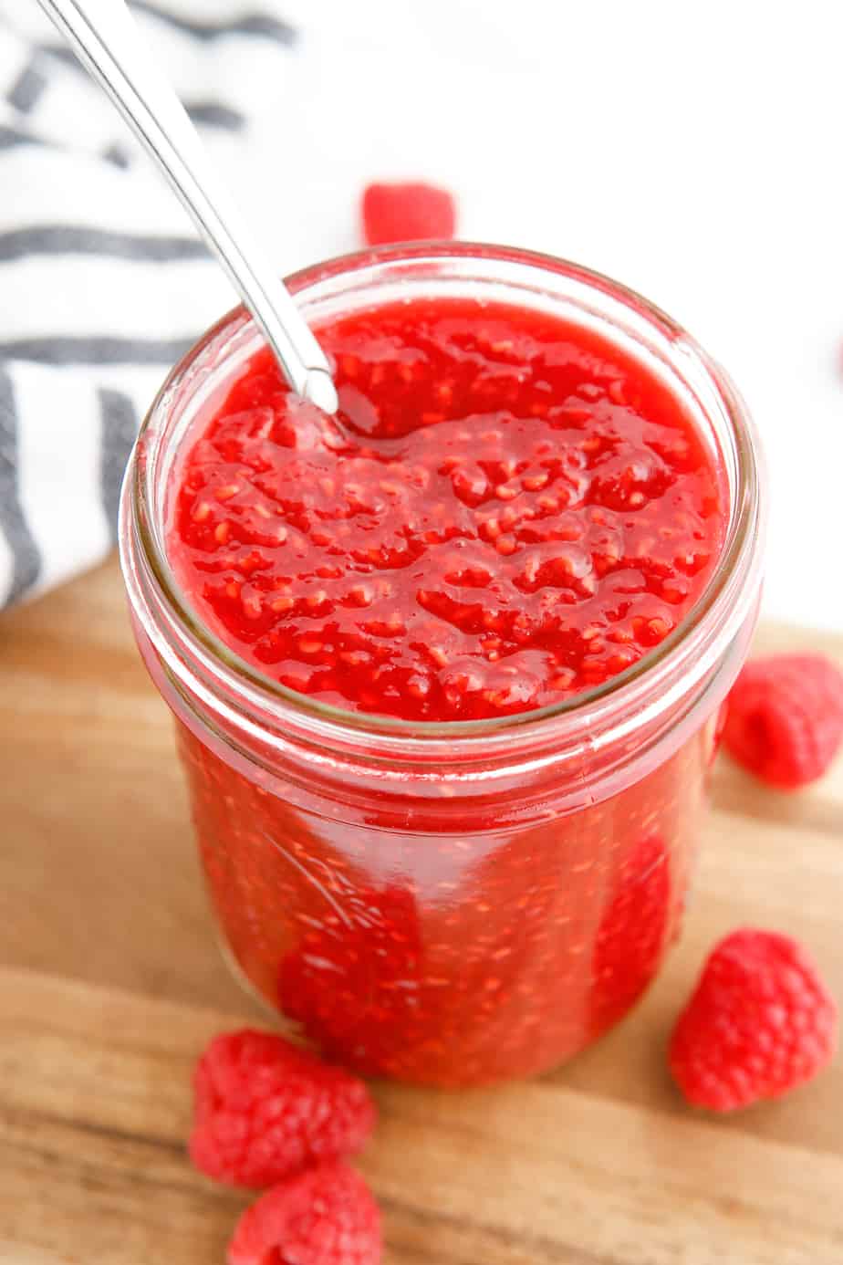 Looking down into a jar of raspberry jam with seeds, and a handle of a spoon sticking out