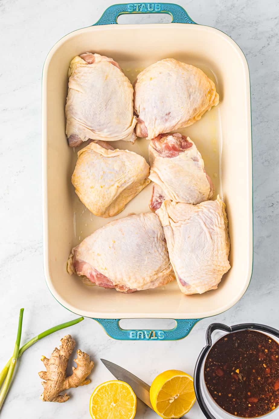 raw bone in chicken thighs lined up in a baking dish with marinade and other ingredients nearby on the table from overhead