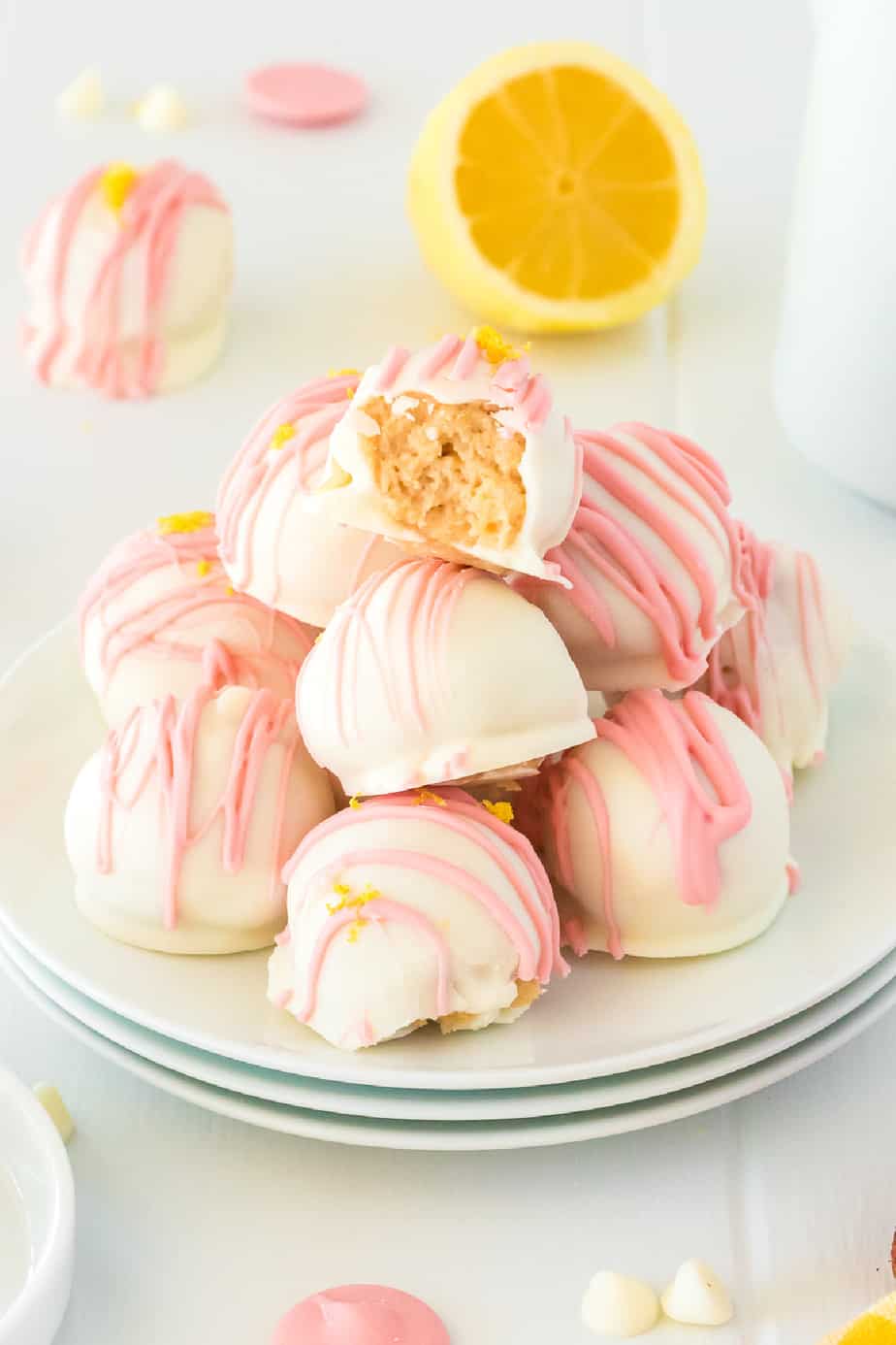 Stack of strawberry lemonade truffles stacked on a plate with the top truffle missing a bite.  Fresh lemon and white chocolate in the background