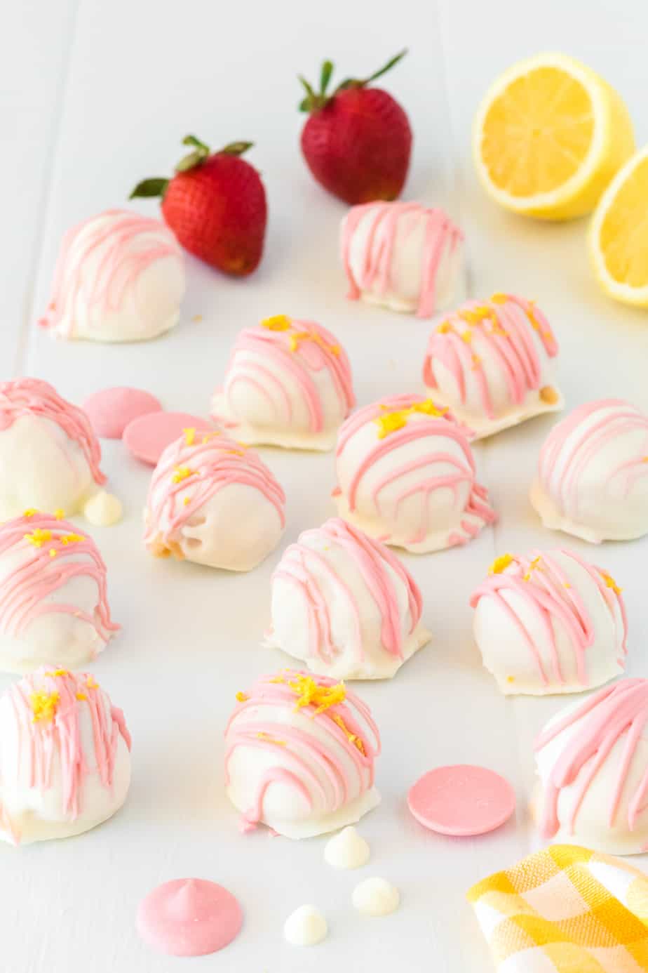 Side view of finished scattered strawberry lemonade truffles on a table with fresh strawberries and lemon nearby