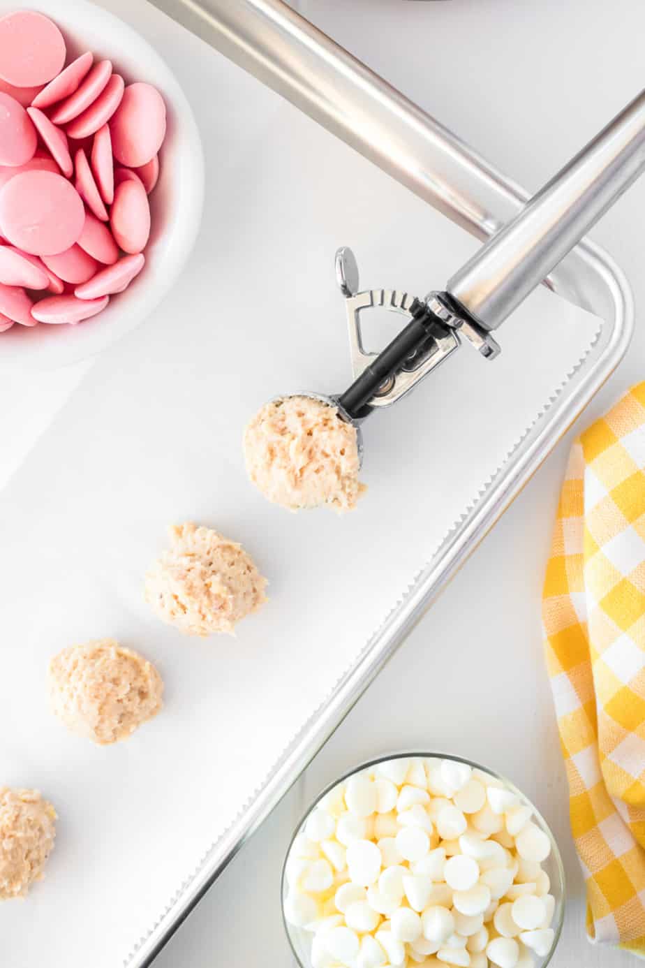 Strawberry lemonade truffles being scooped from a bowl onto a pan with bowls of white chocolate and pink chocolate nearby