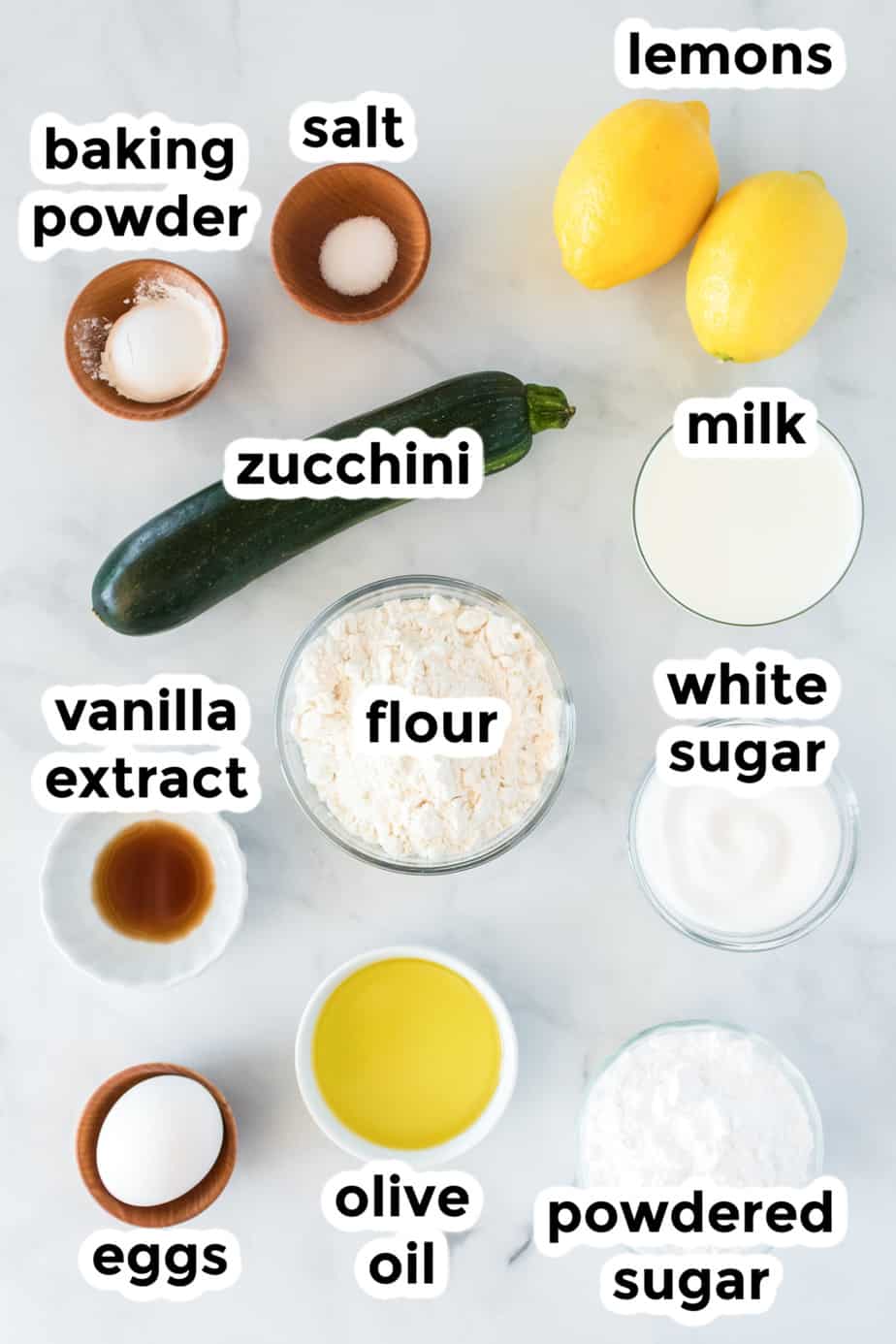 Lemon zucchini cake ingredients in bowls on a counter from above with labels