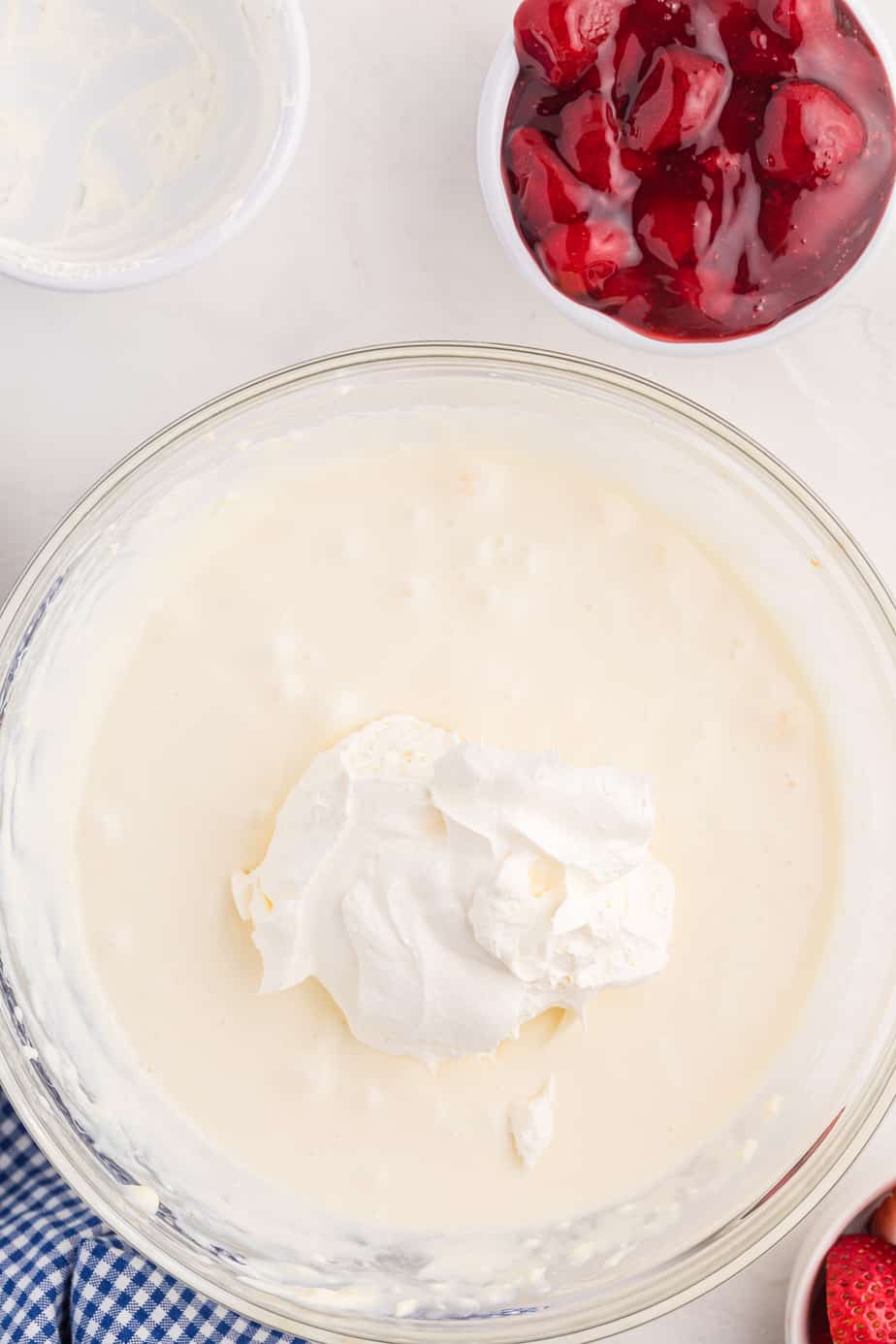 Folding whipped topping  into the cream cheese mixture in a large mixing bowl from overhead with strawberry pie filling in a bowl nearby