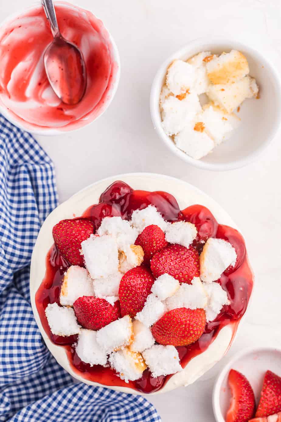 Cheesecake dip topped with strawberry pie filling, angel food cake pieces and fresh strawberries in a serving bowl from above