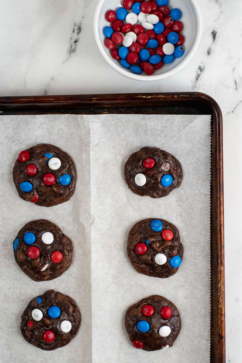 Adding red white and blue MM candies on top of freshly baked brownie cookies on a pan to decorate from above on a counter.