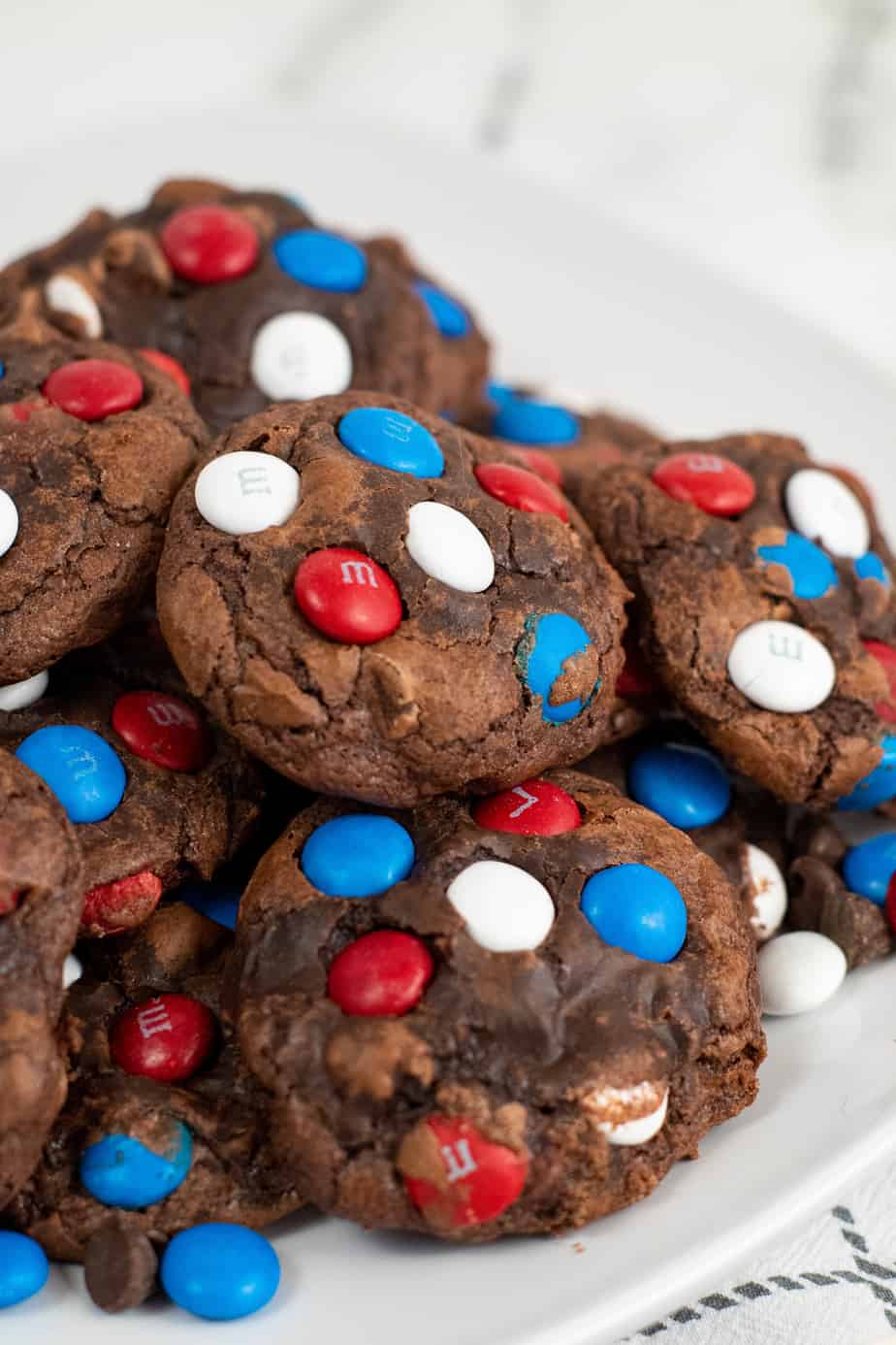 Brownie mix chocolate cookies piled high on a plate with red white and blue MMs in the cookies close up.