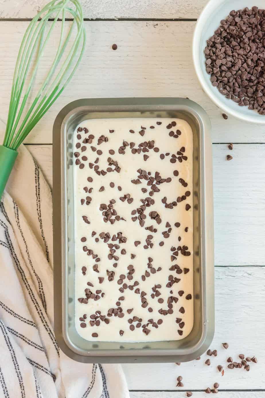 Chocolate chip ice cream in a loaf pan with more chocolate chips sprinkled on top from a bowl nearby.