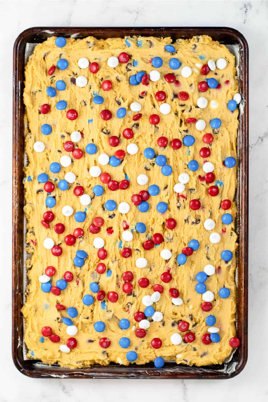Cookie dough pressed into a baking pan topped with red, white and blue MM candies from above.