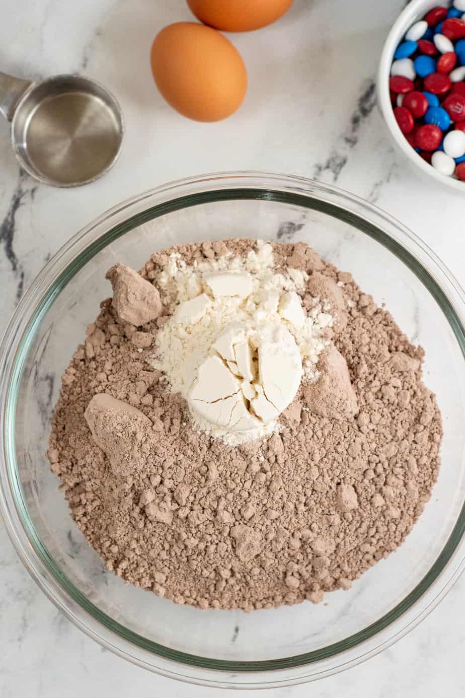 Mixing dry ingredients together in a bowl for brownie cookies from overhead with eggs and MMs in a bowl on the counter nearby.