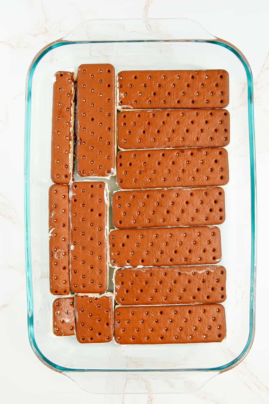Ice cream sandwiches laid in a rectangular pan with some ice cream sandwiches sliced to fit in an even level in the pan from overhead.