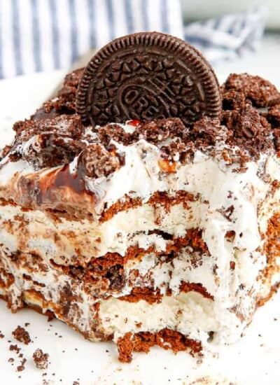 Slice of cookies and cream ice cream cake with a bite missing at the corner showing the ice cream sandwich layers.