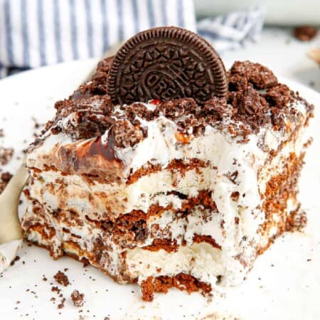 Slice of cookies and cream ice cream cake with a bite missing at the corner showing the ice cream sandwich layers.