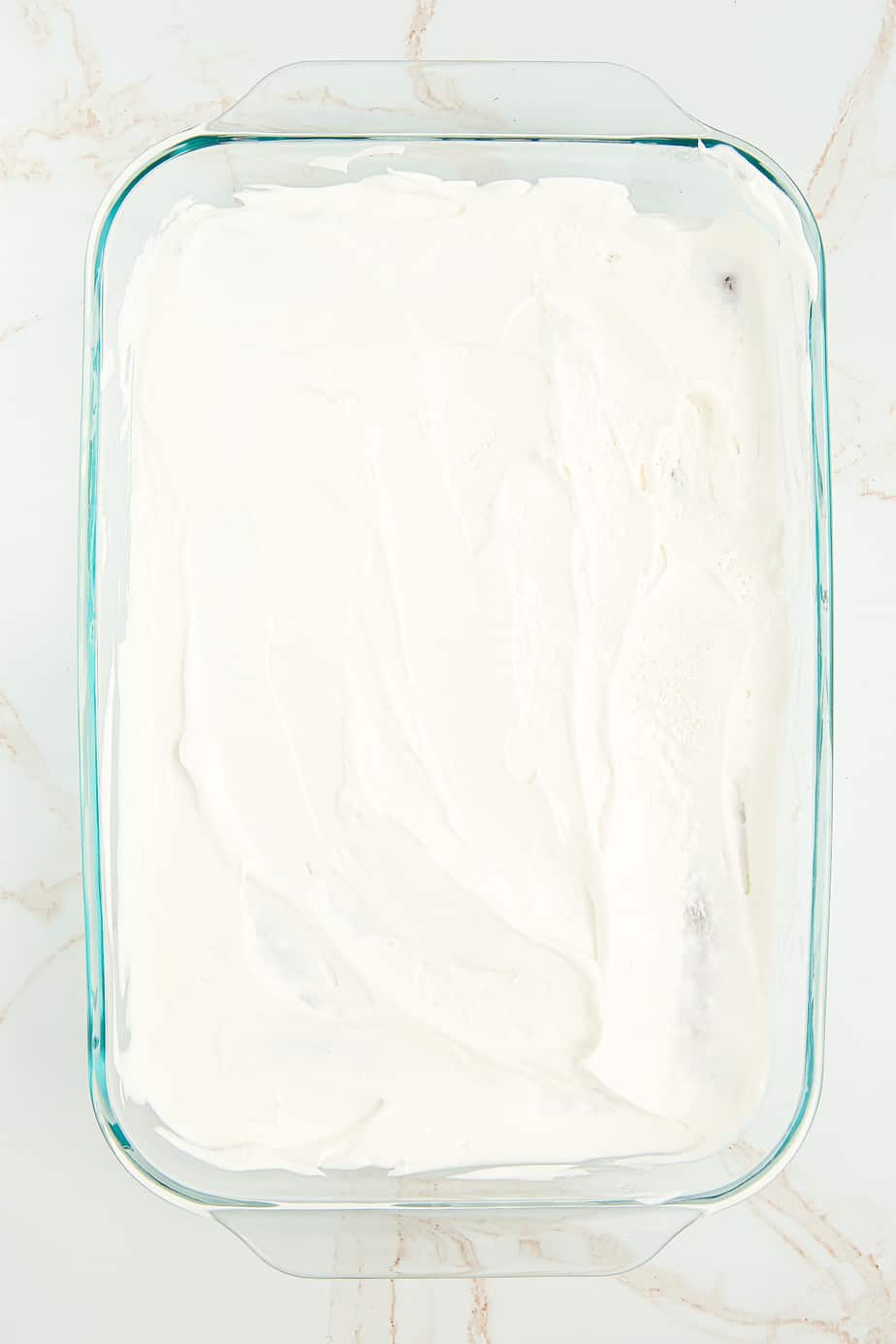 Whipped cream layer spread on top of the ice cream sandwiches in a rectangular pan from overhead.