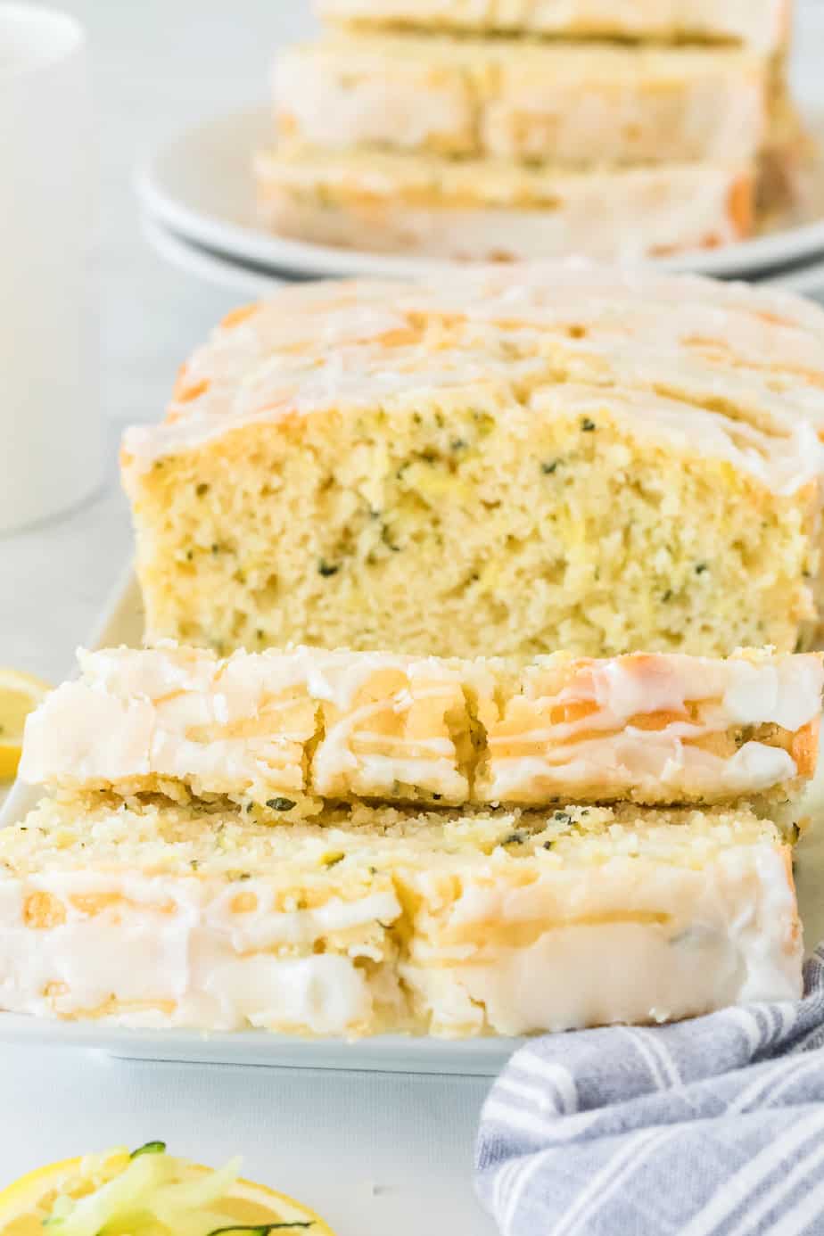 Lemon zucchini cake sliced from a large loaf with glaze on top and zucchini speckled in the cake crumb