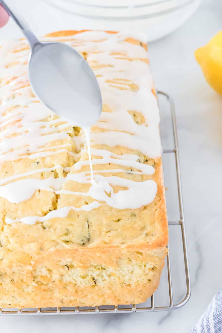 Drizzling lemon glaze with a spoon over the zucchini cake