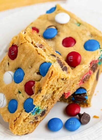 Stack MM cookie bars on plate from side with more red white and blue MMs next to the bars.