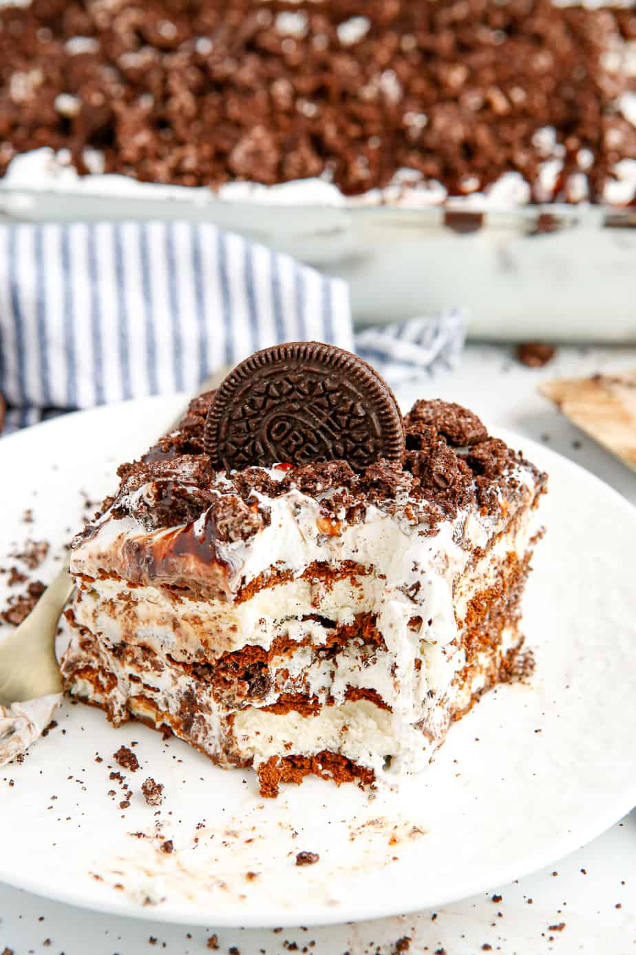 Slice of ice cream cake topped with an Oreo on a plate with a bite missing and you can see all the chocolate layers from the side.
