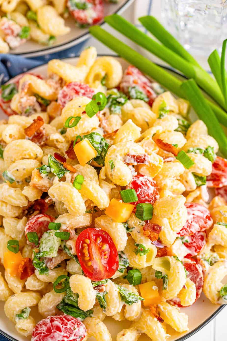 Zoomed in of creamy bacon ranch pasta salad on a plate with a bowl of pasta salad in the background.