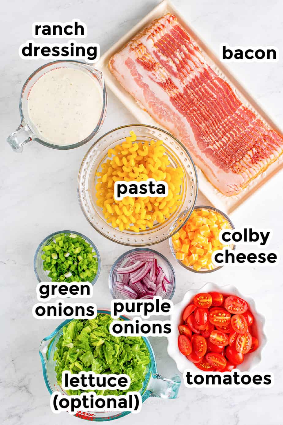 Bacon ranch pasta salad ingredients in bowls with labels from overhead on a counter.