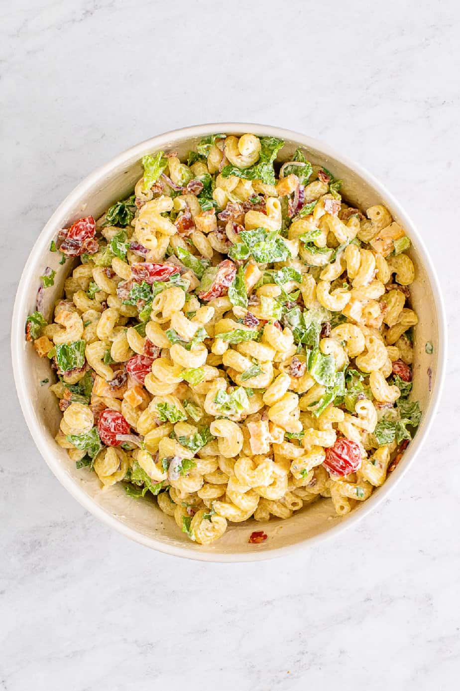 Bacon pieces and lettuce mixed into the bacon ranch pasta salad in a large bowl from overhead on the counter.