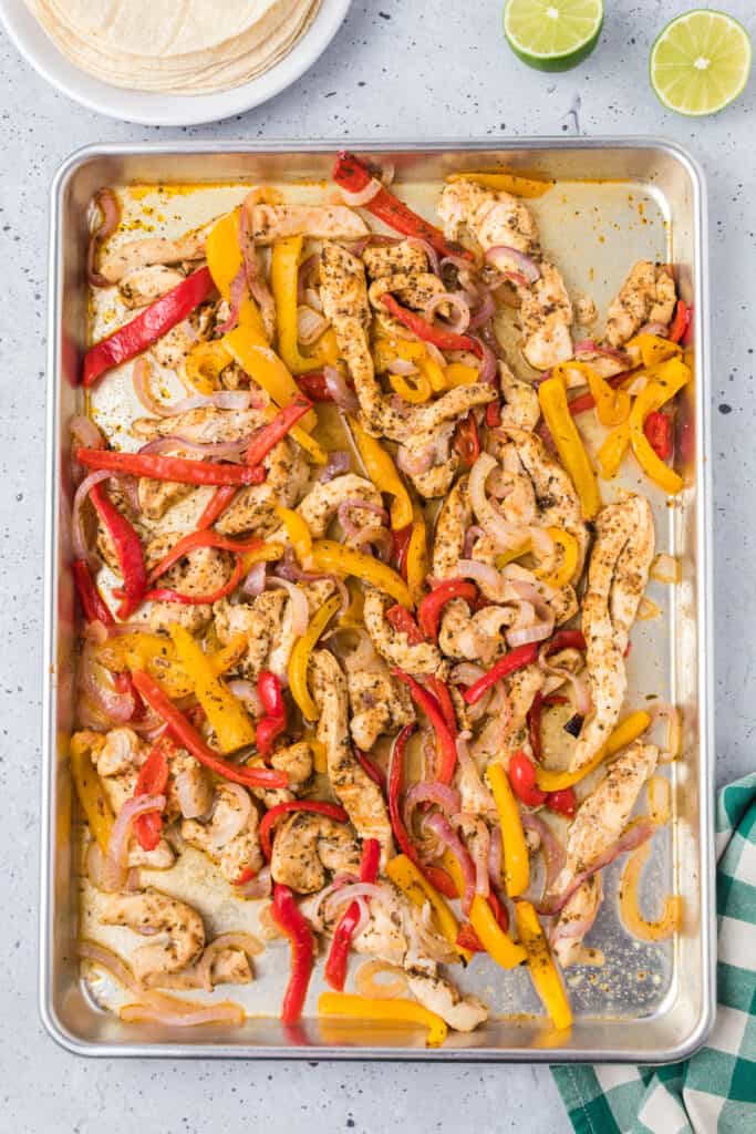 Cooked chicken fajitas slices with peppers and onions on a sheet pan.