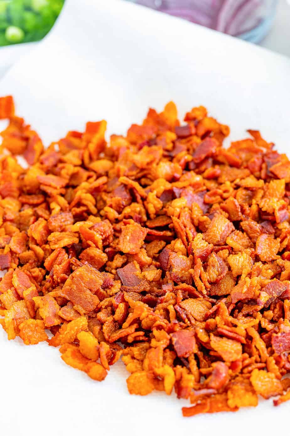 Crispy bacon chopped into small pieces draining on a paper towel from the side.