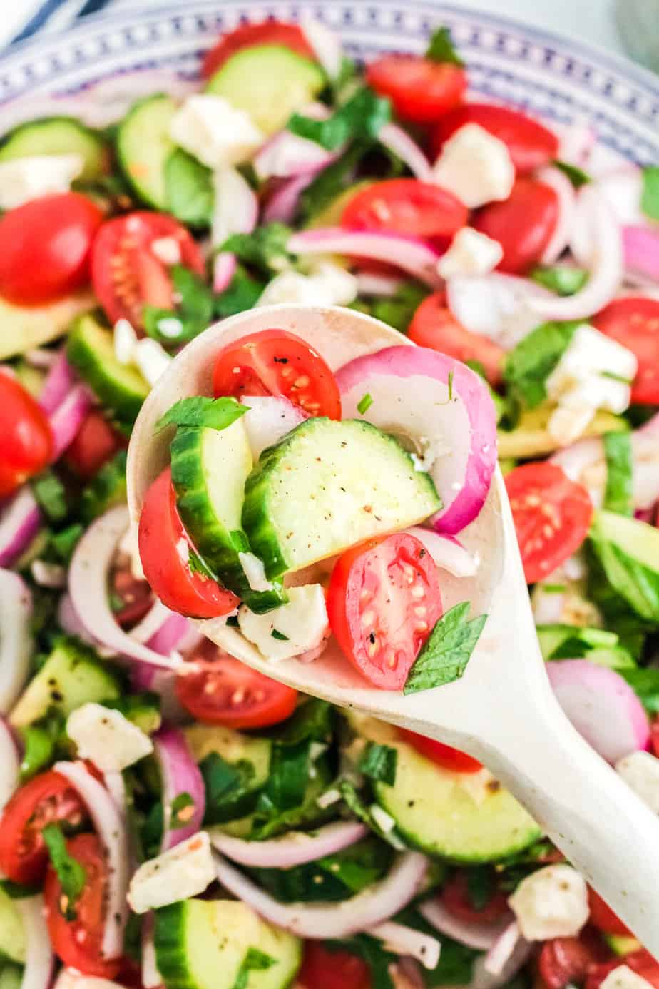 A wooden spoon scooping cucumber tomato salad salad from a bowl up close from overhead.
