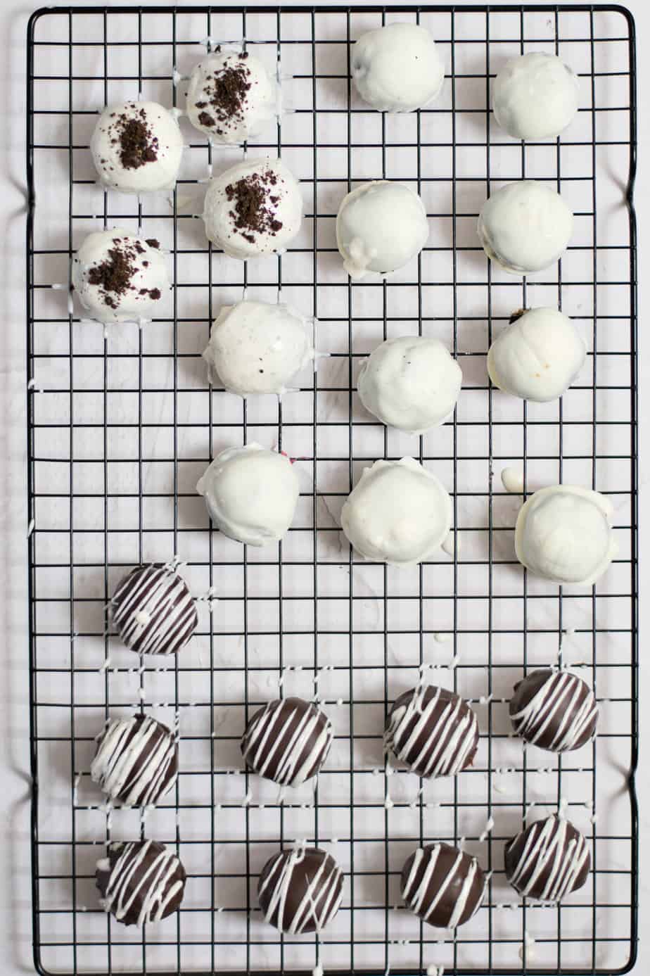 Oreo balls on a wire rack from above, some dipped in chocolate and some dipped in white chocolate with various Oreo crumb and chocolate drizzle toppings.