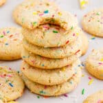 Square view of a stack of funfetti sprinkle cookies with the top cookie missing a bite and more cookies scattered next to the stack.