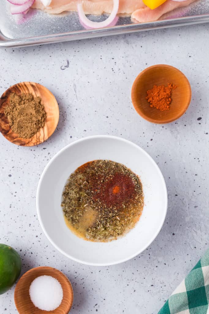 Oil and faijita spices being mixed together in a bowl with small bowls full of spices nearby.