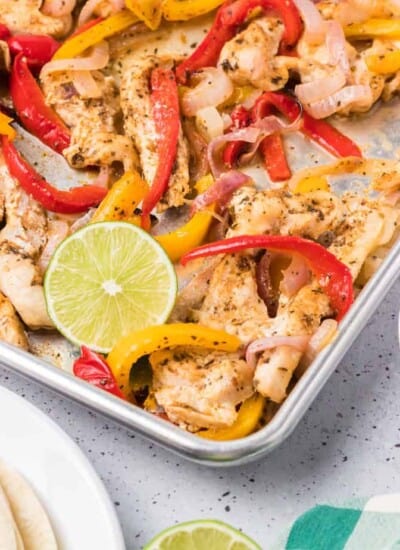 Chicken fajitas on an angled sheet pan with tortillas and salsa next to the pan.
