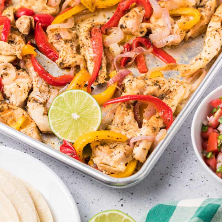 Chicken fajitas on an angled sheet pan with tortillas and salsa next to the pan.