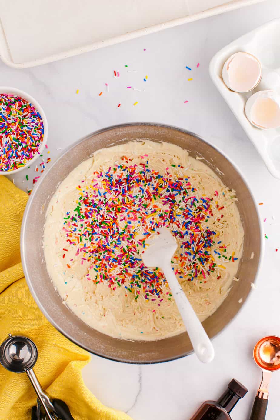 Mixing sprinkles into the funfetti cookie dough in a mixing bowl from above on a counter.