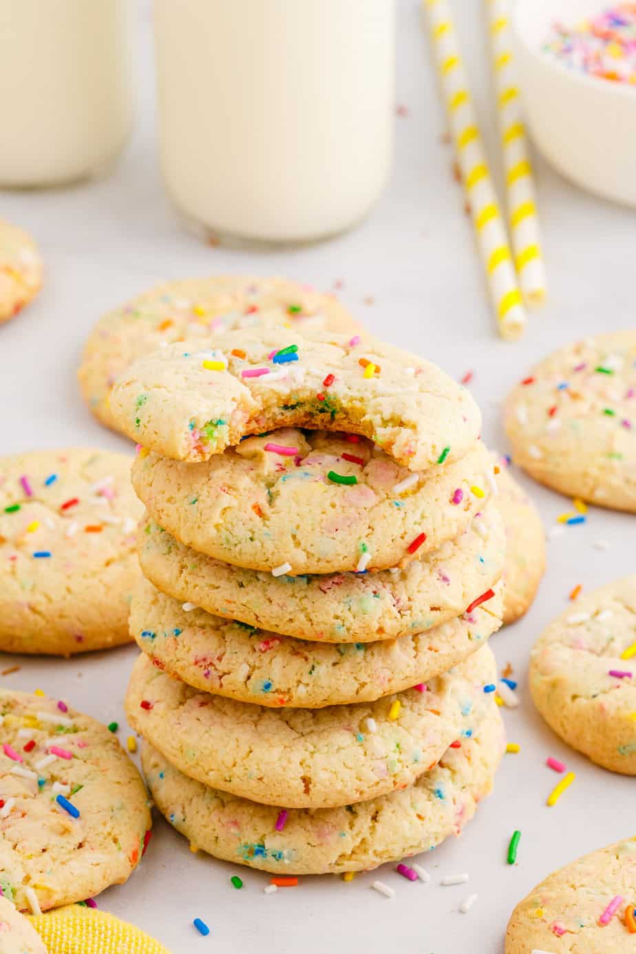 A tall stack of funfetti cake mix cookies from the side on a counter with the top cookie missing a bite and more cookies scattered around the counter.